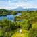 An aerial view of 3 people waving in a lush landscape with a lake and a mountain in the distance